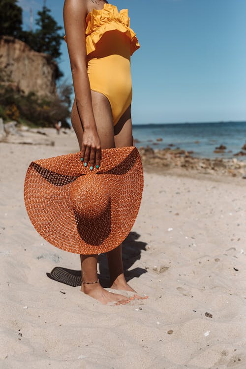 Woman in Yellow Swimsuit and Brown Sun Hat Standing on Beach