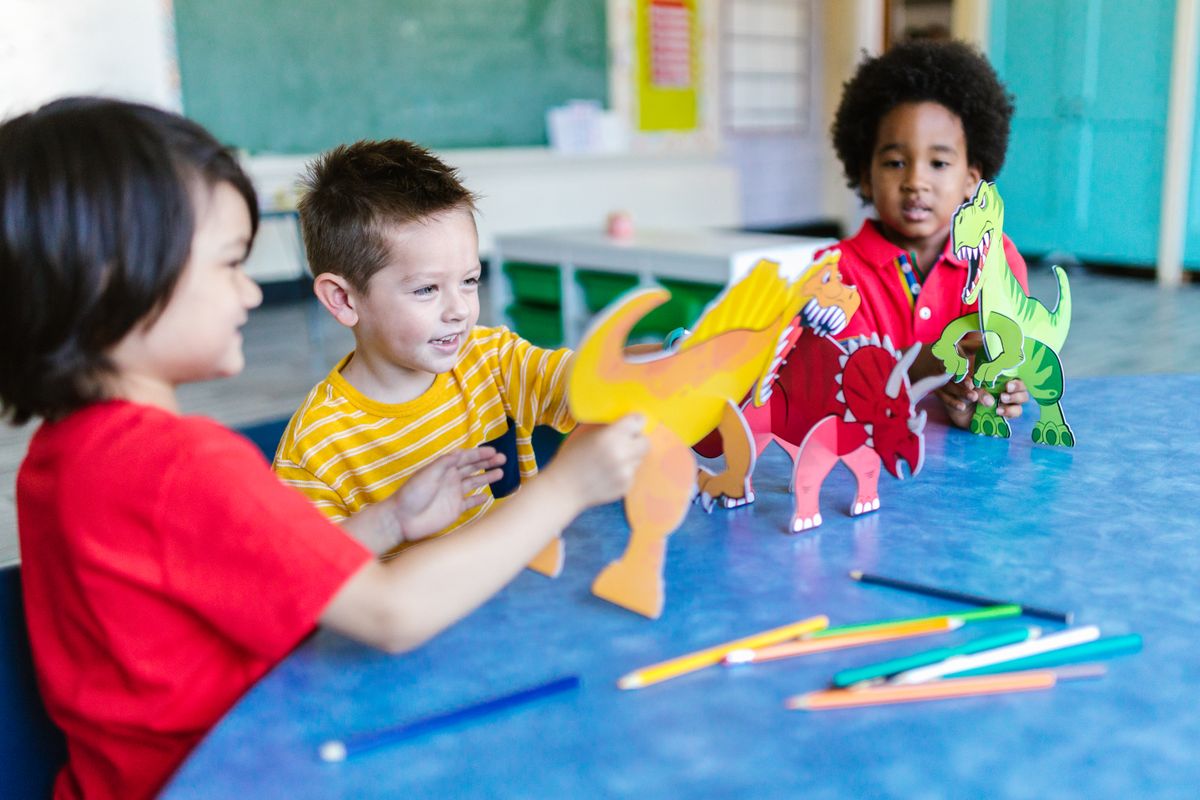 Three kids playing with dinosaur figures before making dinosaur track paintings