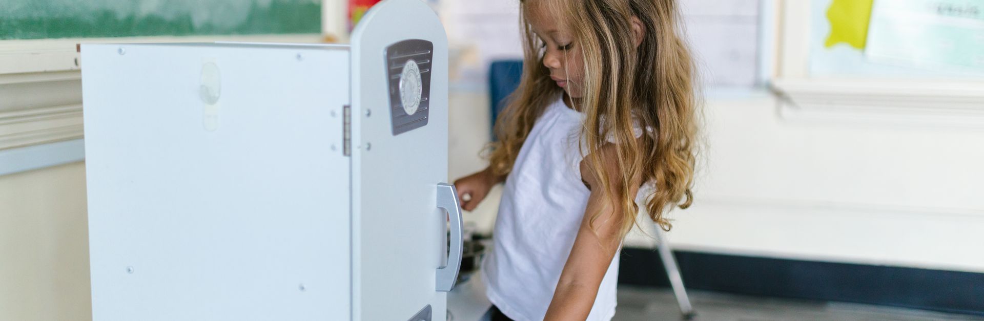 Young girl enjoying playtime in a preschool classroom with toy kitchen appliances.