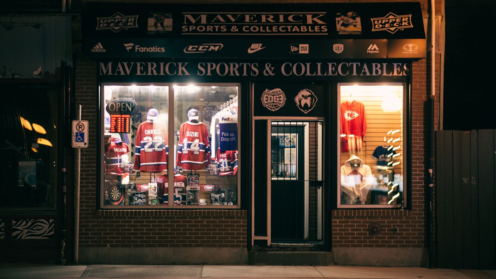 Nighttime view of Maverick Sports & Collectables shop displaying sports jerseys and memorabilia.