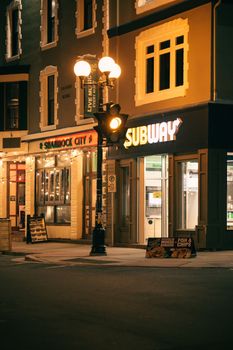 Cozy night scene of a city street featuring illuminated shops and vintage street lighting.