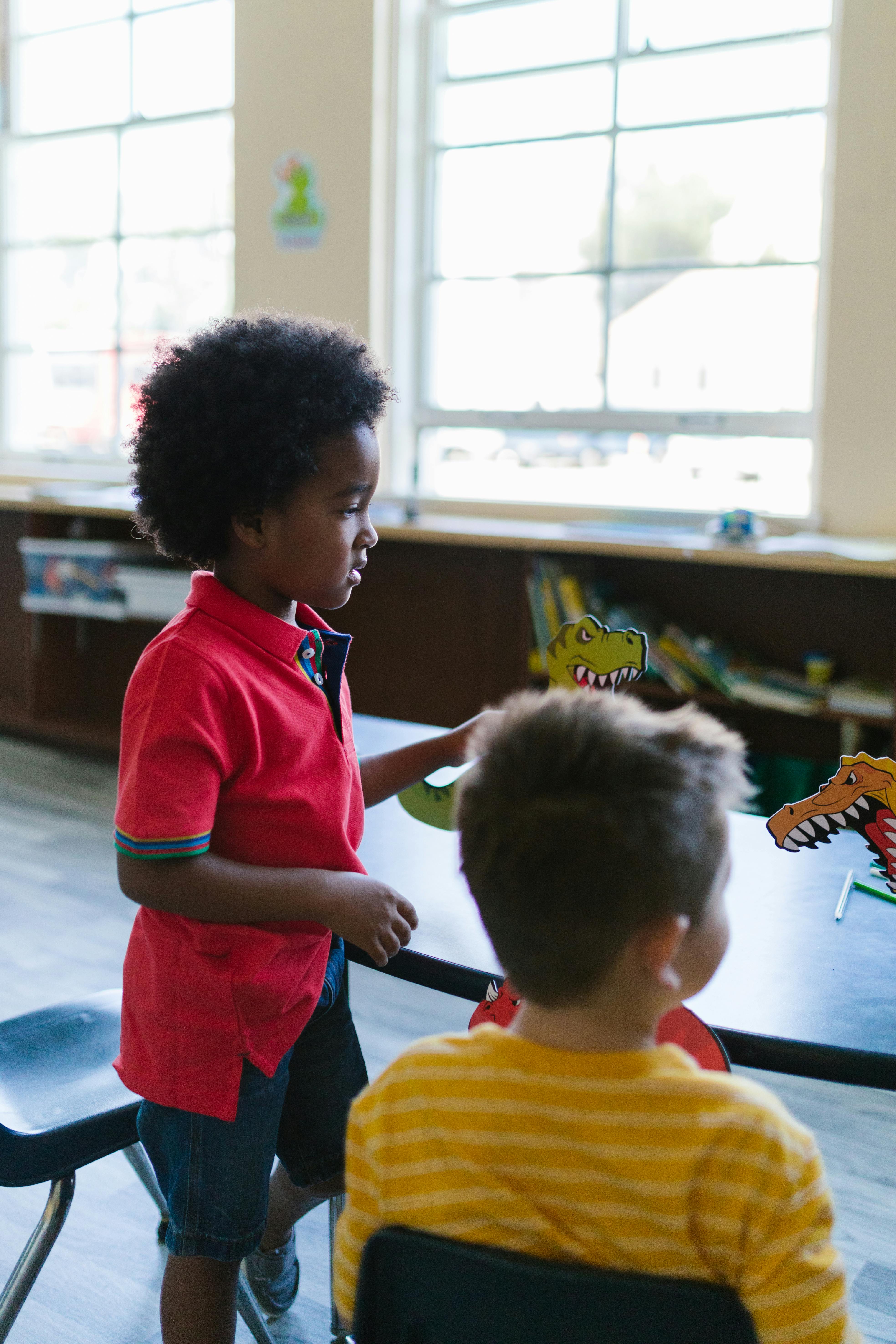 boy in red polo shirt standing beside boy in yellow shirt and playing with dinosaur figures