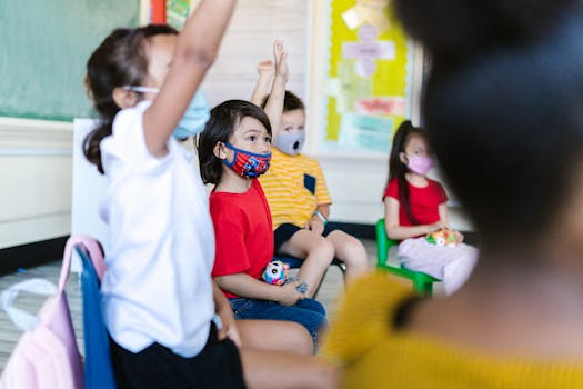 Diverse children in a classroom wearing masks and participating actively by raising their hands.