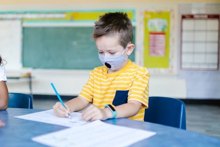 Boy In Yellow And Blue Striped T-Shirt And Face Mask Drawing On White Paper