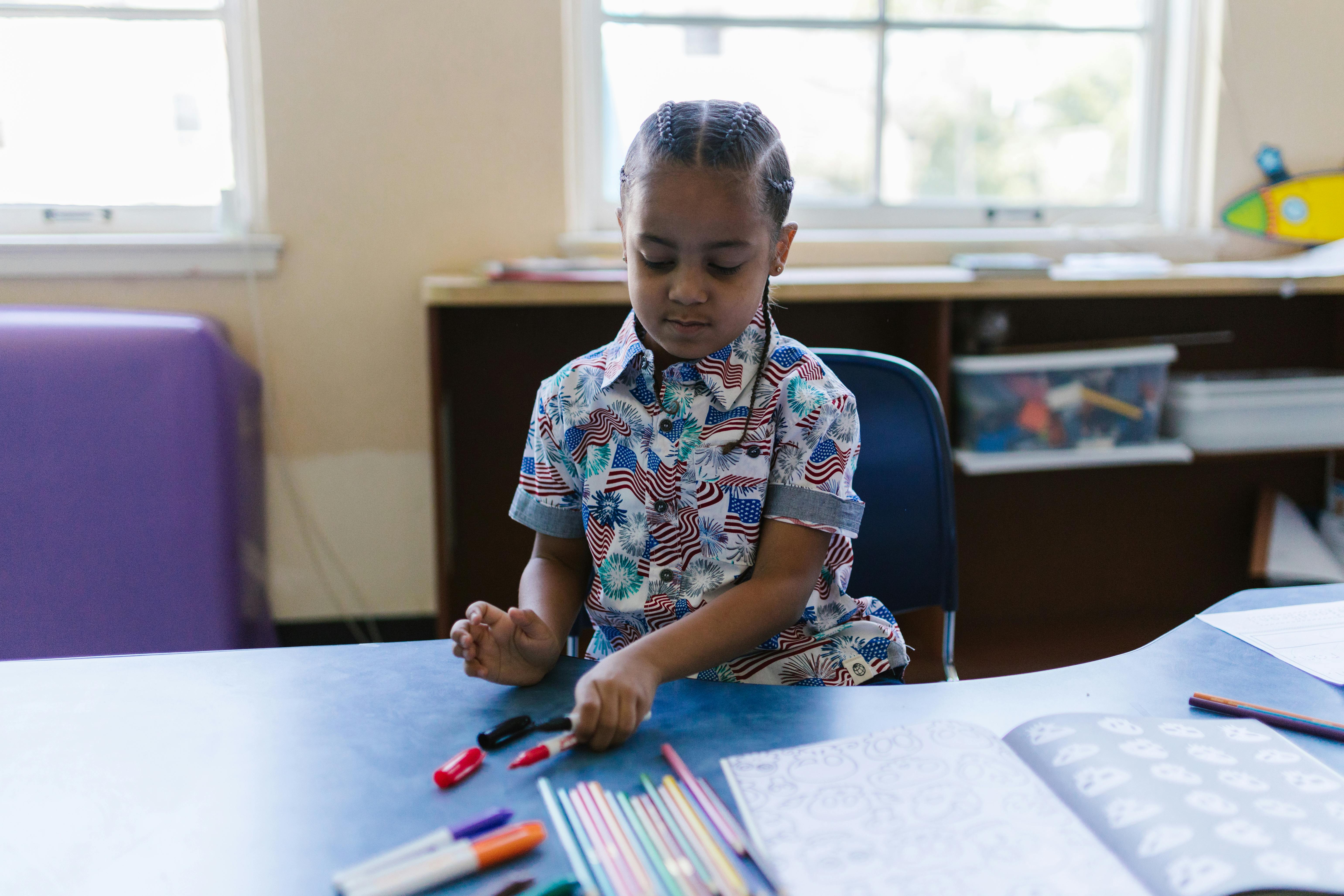 A young boy thoughtfully organizing colored markers at a school desk. | BocaVibe