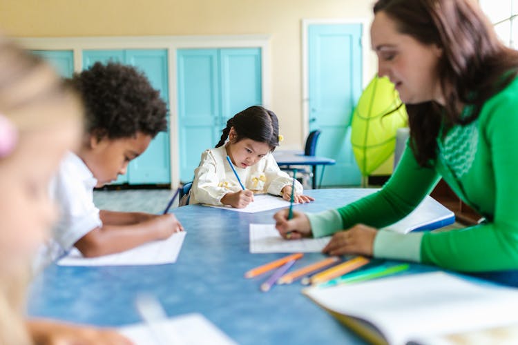 A Woman In Green Long Sleeves Teaching Kids In School