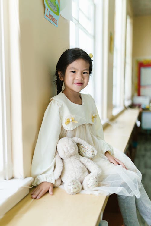 Girl in White Dress Sitting with Bunny on Windowsill