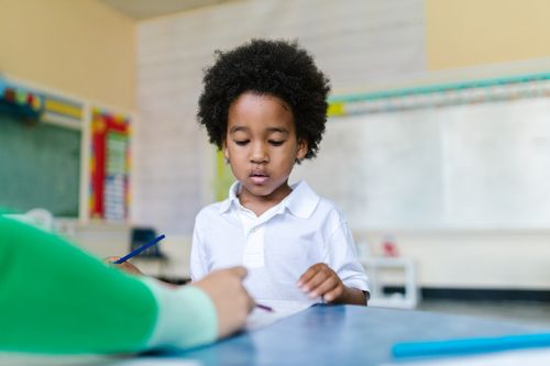 Free A young boy with afro hair learning in a bright classroom setting, engaged in a task. Stock Photo