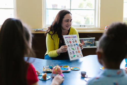 Free Woman in Yellow Long Sleeve Shirt Showing Letters on a Book to Kids Stock Photo