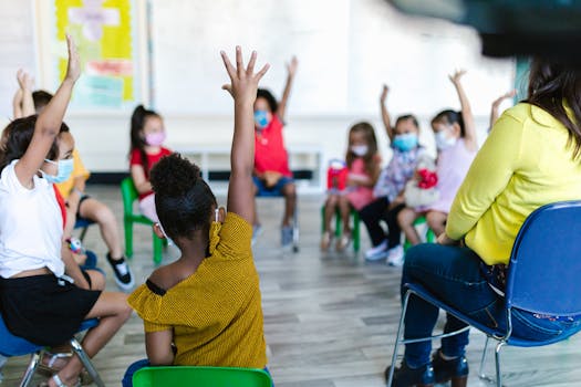 Children in a preschool classroom raise hands during a lesson on a school day, emphasizing diversity and learning.