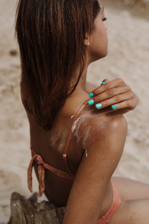 Free Woman Putting Sunblock on Back  Stock Photo