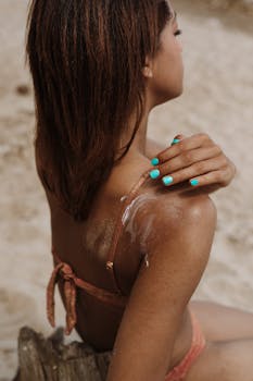 Close-up of woman in swimsuit applying sunscreen on shoulder at the beach.