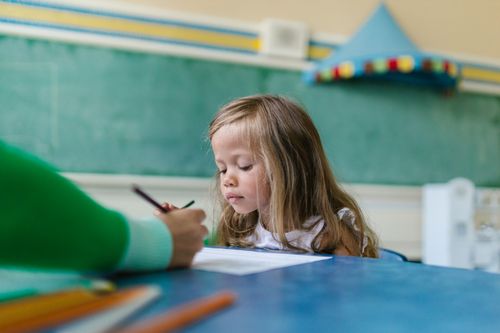 Free A young girl with long hair concentrates on her drawing in a colorful classroom environment. Stock Photo