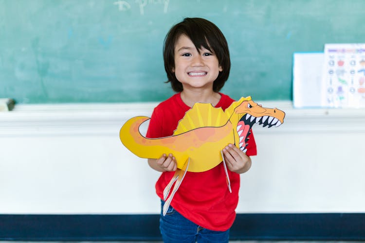 A Young Boy Smiling While Holding A Dinosaur Cutout