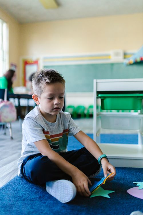 Free A young boy sits on a carpet engrossed in play within a preschool classroom, creating a learning atmosphere. Stock Photo