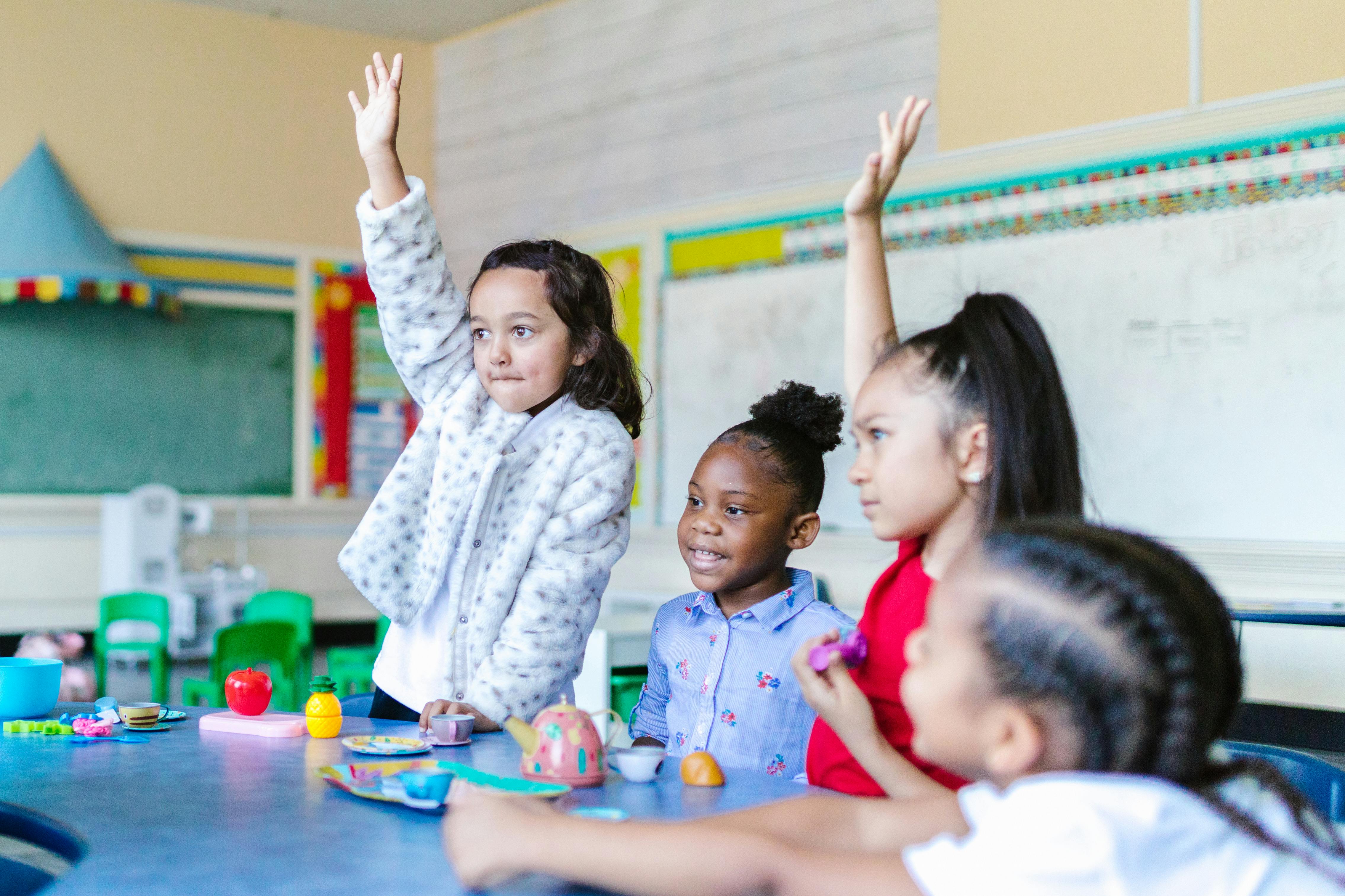 Multicultural group of kids eagerly participating in a classroom setting, raising hands with smiles.