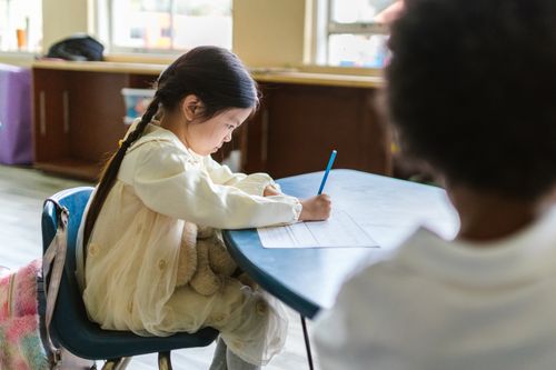 Free A young child intensely focused on writing at a classroom table, showing concentration and learning. Stock Photo