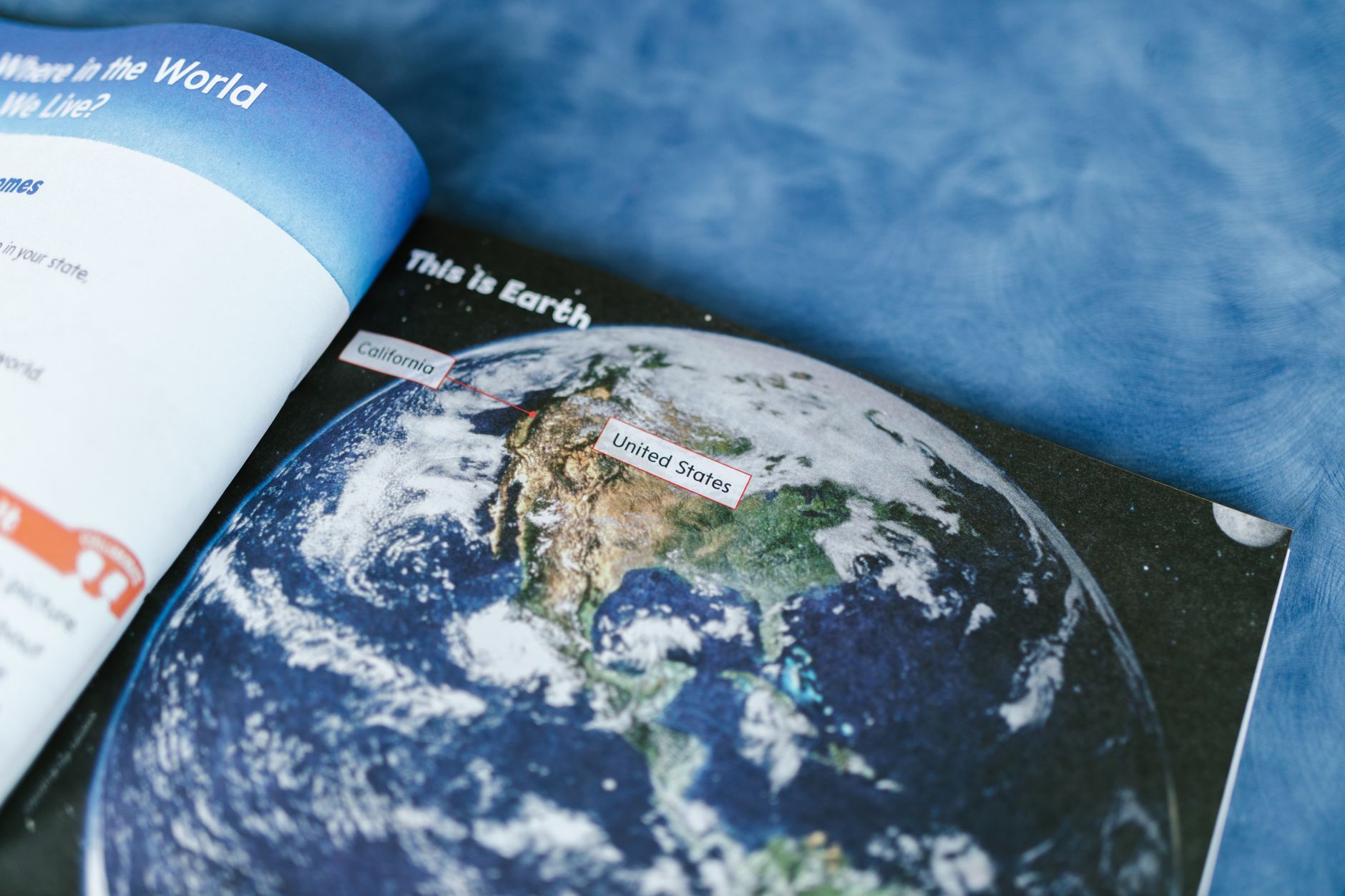 Open educational book showing an Earth illustration on a blue textured surface.