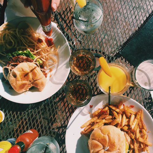Free Casual outdoor dining setup with burgers, fries, pasta, and drinks on a mesh table. Stock Photo