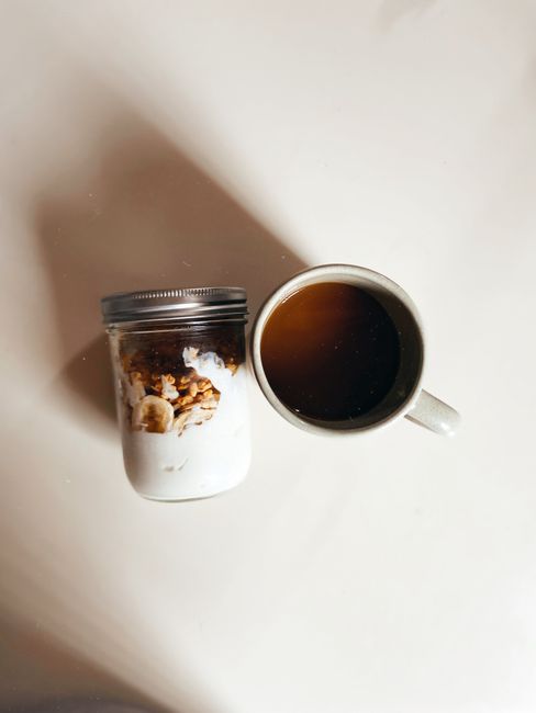A nutritious breakfast setup with a cup of black coffee and a mason jar filled with granola and yogurt.