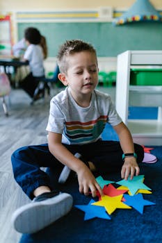 Young boy in preschool playing with colorful paper stars in a classroom setting.