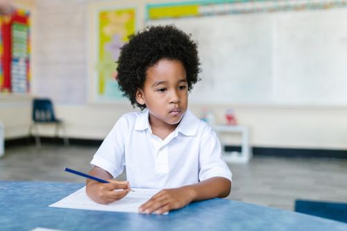 Free A focused young boy with afro hair writing in a classroom setting, showcasing education and learning. Stock Photo