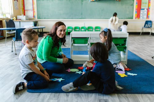Woman Sitting Beside Children Inside the Classroom
