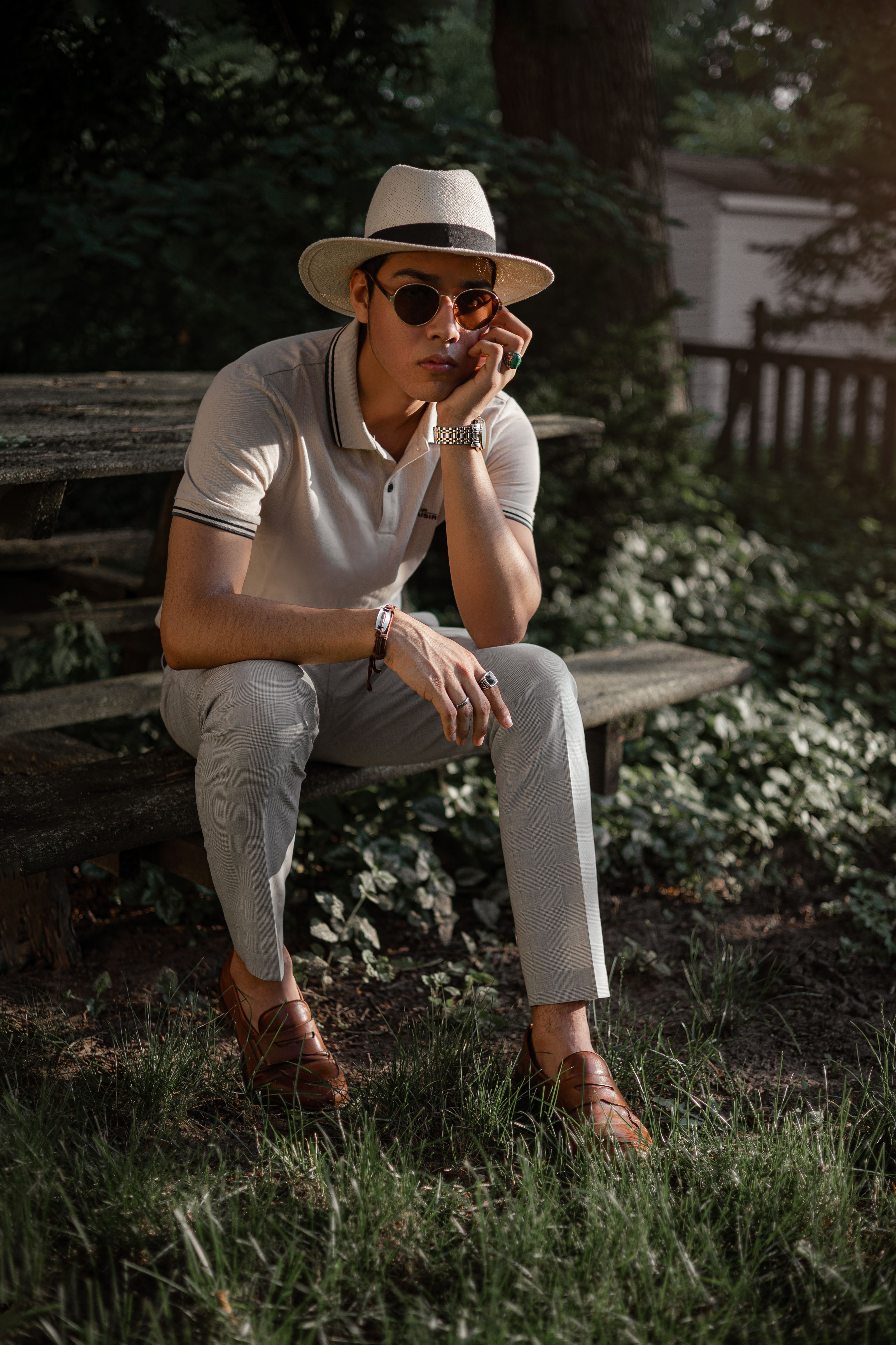 Homem fashion com chapéu e óculos de sol posando ao ar livre em um dia ensolarado.