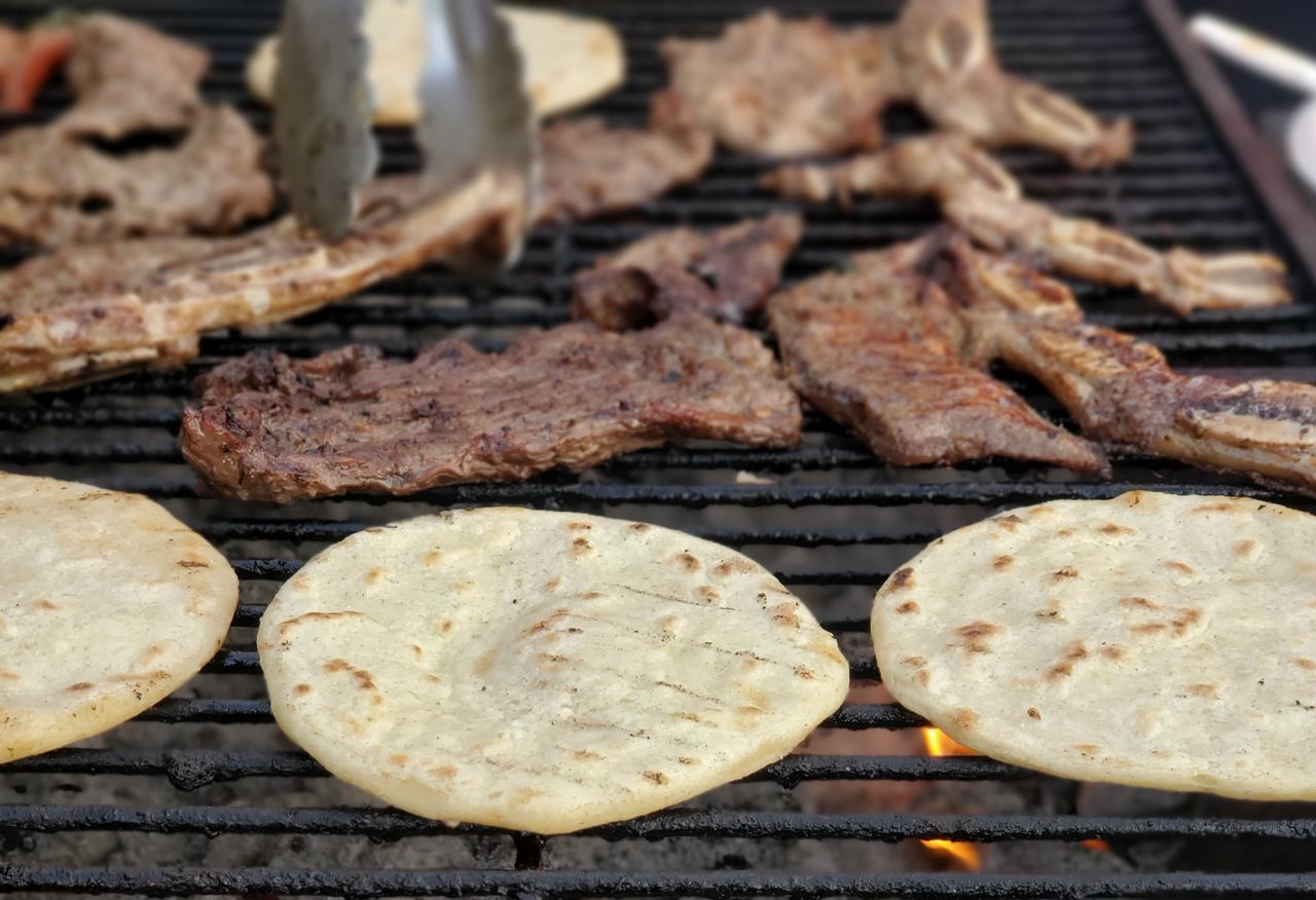 Sizzling meat and tortillas grilling on a hot barbecue with smoke rising