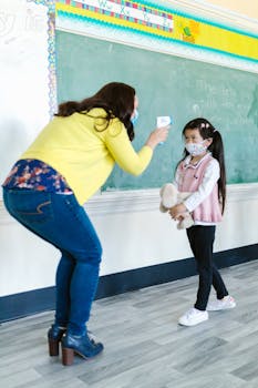 A teacher checks a student's temperature in a classroom setting during the pandemic.