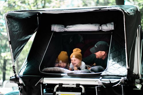 Free A father and his children enjoy laughter and togetherness in a rooftop tent during a summer camping trip in the woods. Stock Photo