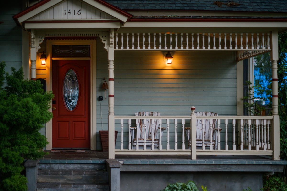 Welcoming front porch with a red door and wooden armchairs at dusk