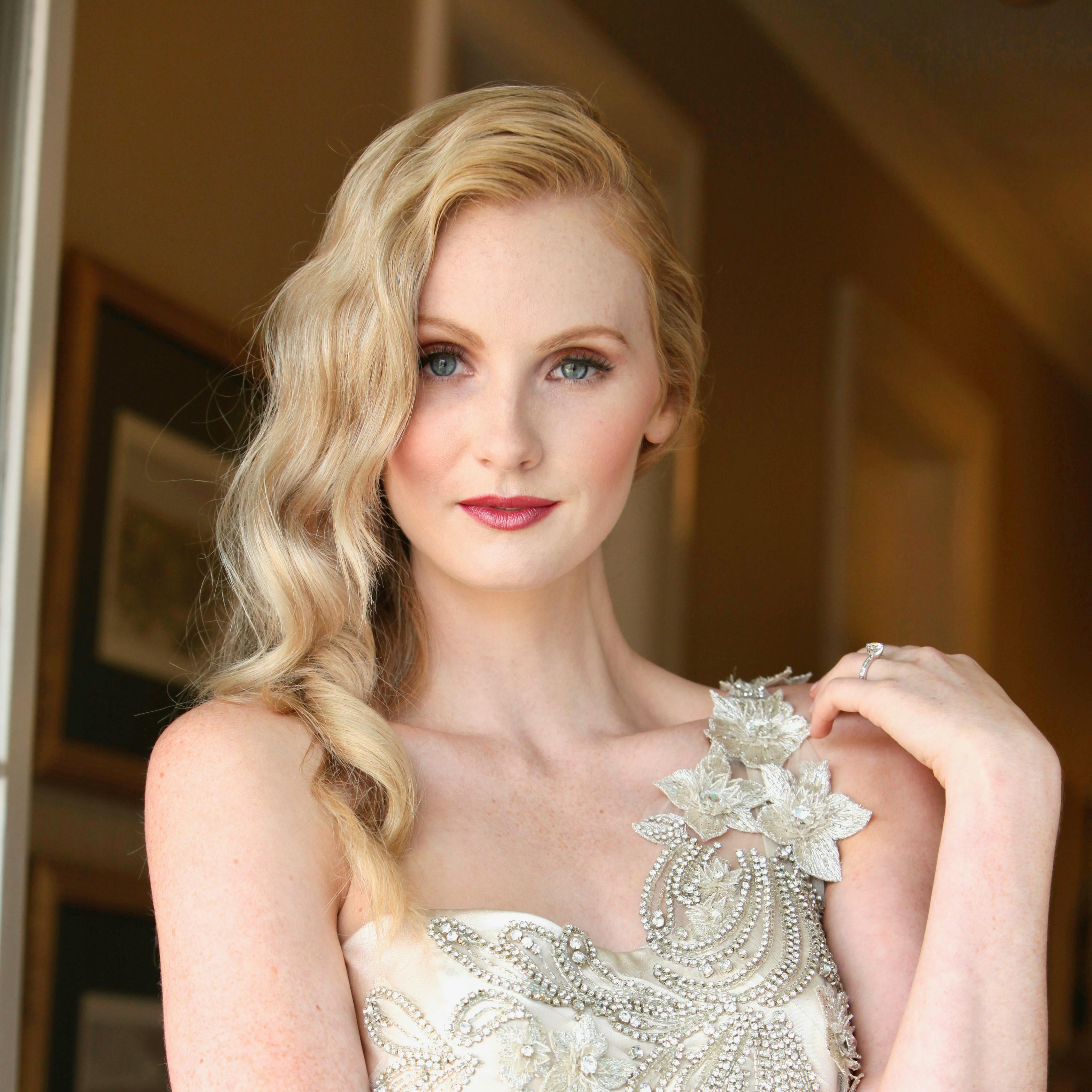 Elegant blonde woman in a stylish gown posing indoors with a confident smile.