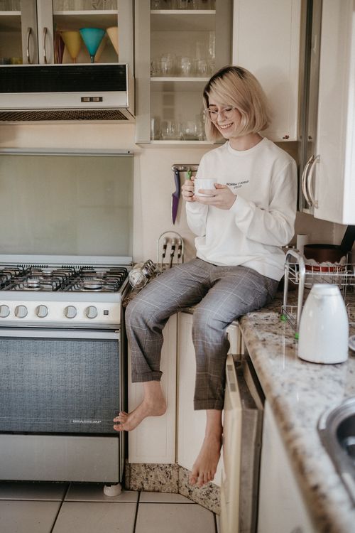 Free A woman enjoys coffee while sitting on a kitchen counter, creating a cozy and warm atmosphere. Stock Photo