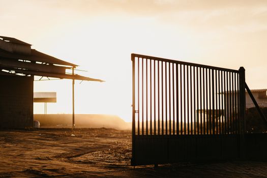 Industrial landscape with a metal gate silhouetted against a sunset sky, exuding a warm, rustic ambiance.