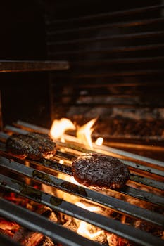Close-up of juicy beef patties grilling over open flames, capturing the essence of outdoor cooking.