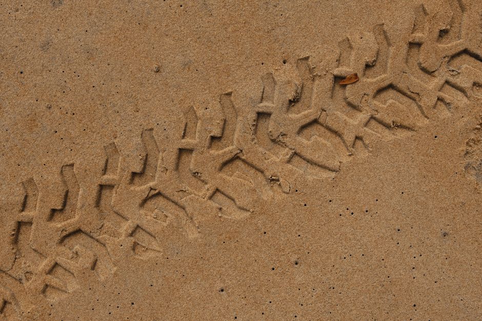 Close-up of tire tracks indented in sandy ground, showcasing pattern and texture.