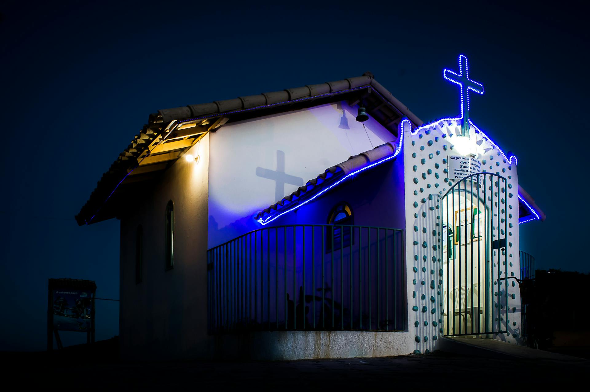 Small chapel with illuminated cross and blue lighting at night, conveying spirituality and peace.