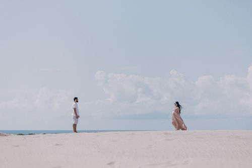 Free A couple standing apart on a peaceful beach with a clear blue sky, capturing serene moments. Stock Photo