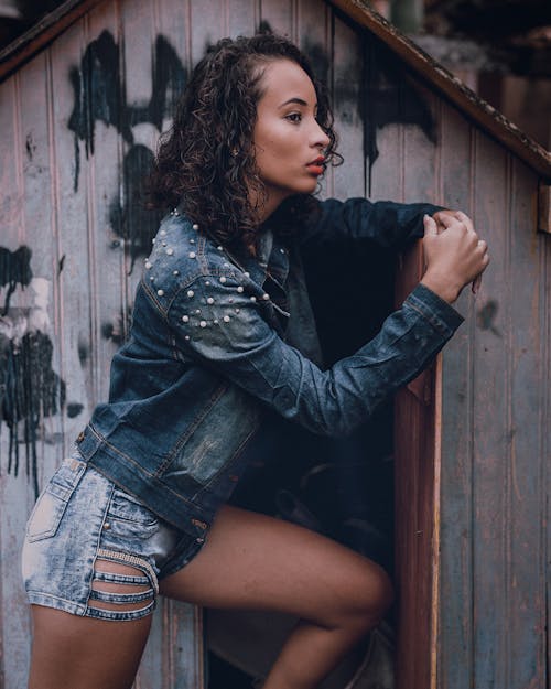 Woman in Denim Outfit Leaning on a Door to Wooden Shed 