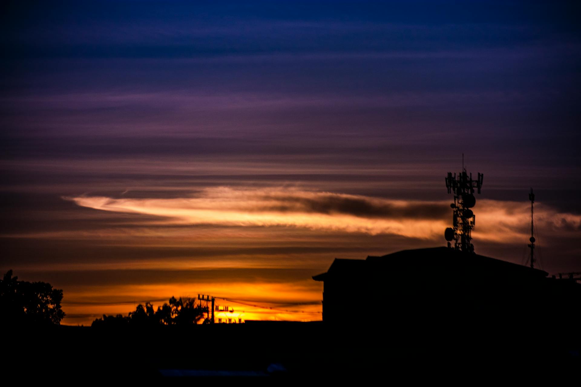 A silhouetted cell tower against a vivid and dramatic sunset sky with clouds.