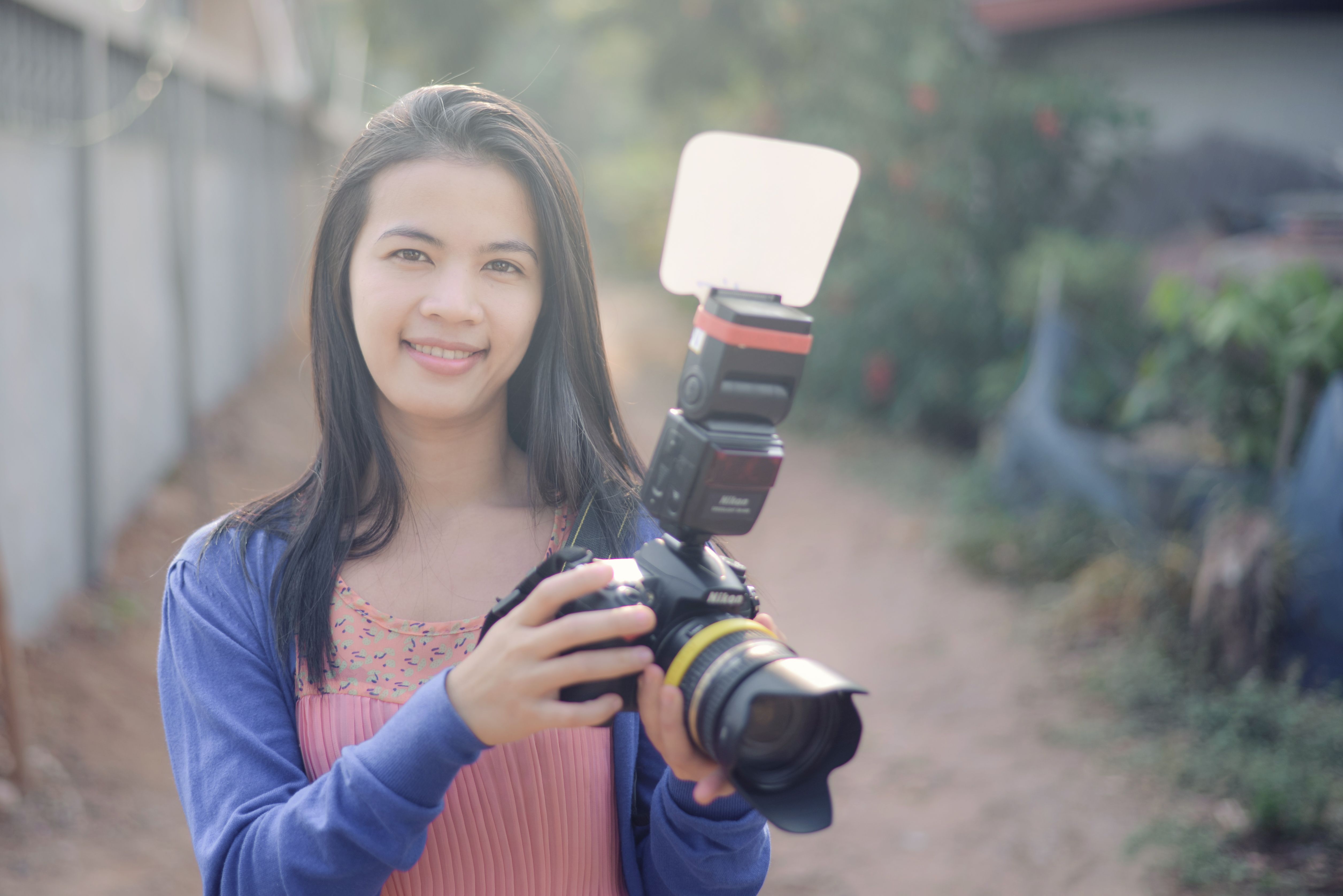 Portrait of a woman smiling and holding a digital camera with flash outdoors.