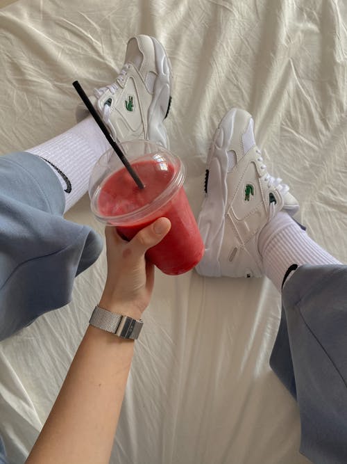 Free A Person Wearing White Shoes while Holding a Smoothie Stock Photo