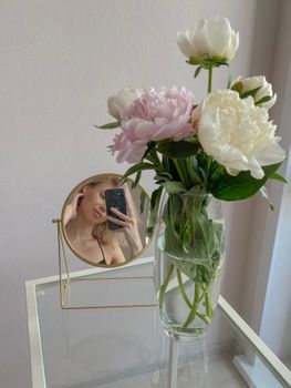 A stylish peony bouquet with mirror reflection capturing a woman taking a selfie.