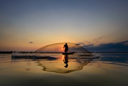 A serene silhouette of a fisherman casting a net on a calm lake at sunrise.