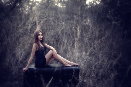 Free A woman in a black dress poses gracefully on a couch amidst a serene outdoor environment. Stock Photo