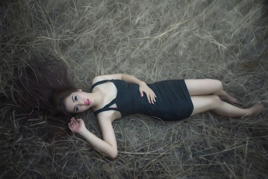 Artistic portrait of a woman in a black dress lying on dry grass outdoors.