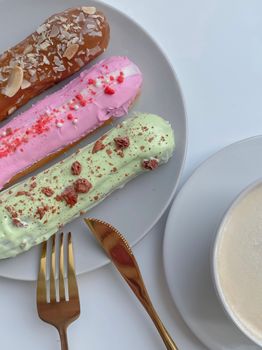 Three vibrant eclairs with toppings alongside a creamy coffee, perfect for dessert lovers.