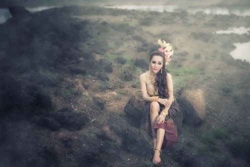 Free A woman in traditional attire sitting elegantly on rocks in a misty outdoor setting. Stock Photo