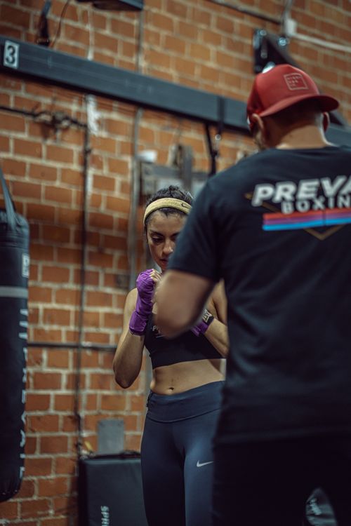 Free Concentrate ethnic female boxer in activewear training with unrecognizable instructor in cap in gym in daytime Stock Photo